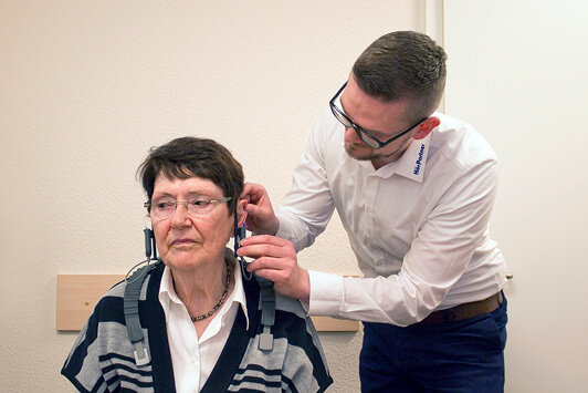 Ein Hörakustiker passt einer älteren Frau ein Hörgerät zur Hörberatung an.