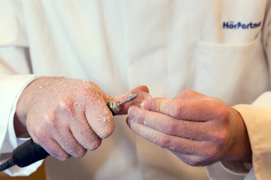 Ein Hörakustiker schleift ein Hörgerät in der Werkstatt für individuelle Anpassung.